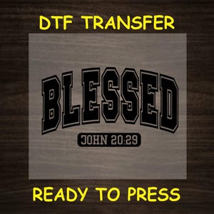 May include: A black and white iron-on transfer design with the word "Blessed" in a bold, varsity-style font. The text "JOHN 20:29" is below the word "Blessed". The design is ready to be pressed onto fabric.