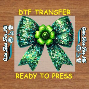 May include: A green sequined bow with a green flower in the center. The text "DTF TRANSFER" and "READY TO PRESS" are in yellow. The words "Cute Tees For All" are on the left and right sides.