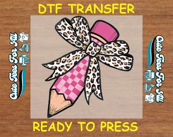 May include: A DTF transfer featuring a pencil with a pink eraser and a bow. The bow has a leopard print pattern. The pencil shaft has a pink and white checkered pattern. The text "DTF TRANSFER" and "READY TO PRESS" are displayed.