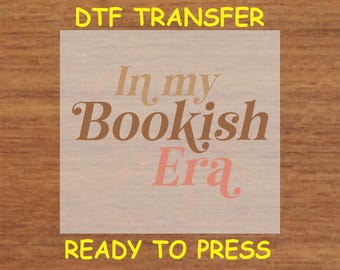 May include: A ready-to-press DTF transfer with the text "In my Bookish Era" in brown and pink lettering on a white background.