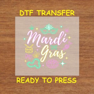 Puede incluir: Una hoja de transferencia DTF con un diseño que dice "Mardi Gras" en letras rosas y amarillas. El diseño incluye una máscara, cuentas, un tambor y otros símbolos de Mardi Gras.