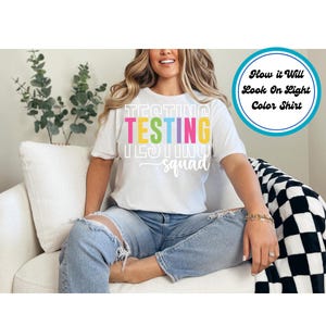 May include: White t-shirt with the text "TESTING squad" in rainbow colors. The text is stacked vertically with the word "TESTING" in larger font. How it will look on a light color shirt.