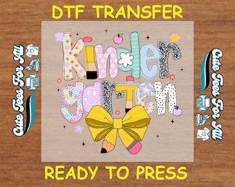 May include: A DTF transfer design with the word "Kindergarten" in colorful, patterned letters. A yellow bow with a pencil accent is at the bottom. The text "DTF TRANSFER" and "READY TO PRESS" are at the top and bottom.