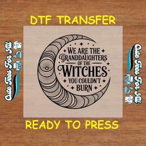 May include: A DTF transfer with the text "WE ARE THE GRANDDAUGHTERS OF THE WITCHES YOU COULDN'T BURN" inside a crescent moon design. The words "DTF TRANSFER" and "READY TO PRESS" are also present. The image has a wooden background.