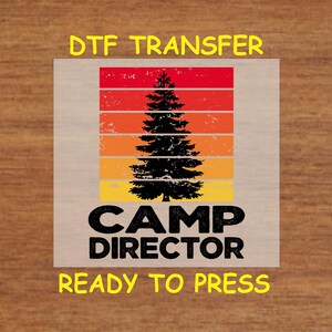 May include: A ready-to-press iron-on transfer design featuring a retro-style sunset with a pine tree and the text "Camp Director".