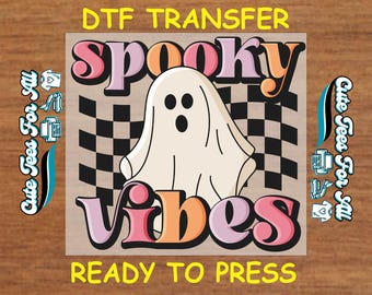 May include: A DTF transfer featuring a cartoon ghost with the words "Spooky Vibes" in pink, orange, and purple. The design includes a black and white checkered background and the text "Ready to Press". The words "Cute Tees For All" are also present.