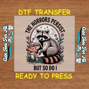 May include: DTF transfer featuring a raccoon with the text "The Horrors Persist But So Do I." The raccoon is surrounded by mushrooms and flowers. The design is ready to press.