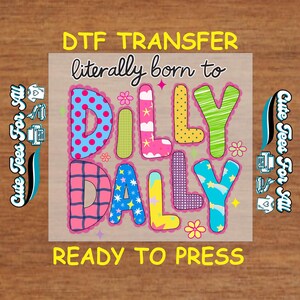 May include: A DTF transfer sheet featuring the text literally born to DILLY DALLY in colorful, patterned bubble letters. The design includes polka dots, plaid, stars, and clouds in blue, pink, yellow, and green. Text reads DTF TRANSFER and READY TO PRESS.
