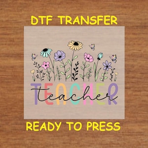 May include: A ready-to-press iron-on transfer design featuring a colorful floral arrangement with butterflies and the word "teacher" in rainbow colors.