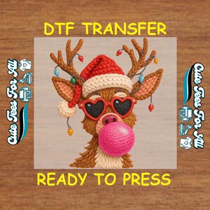 May include: A whimsical DTF transfer featuring a reindeer with a Santa hat, heart-shaped sunglasses, and a pink bubble. The design includes the text "DTF TRANSFER" and "READY TO PRESS" in yellow.