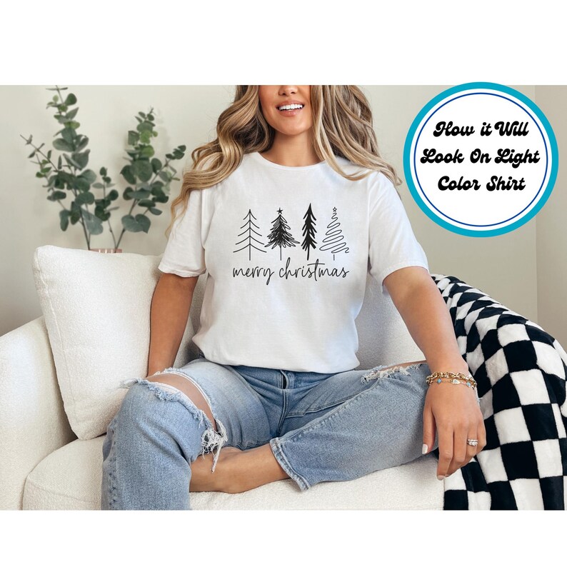 Puede incluir: Camiseta blanca con un dibujo lineal negro de cuatro &aacute;rboles de Navidad y la frase "merry christmas" en fuente manuscrita. La camiseta es de color claro y tiene mangas cortas.