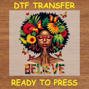 May include: A ready-to-press iron-on transfer featuring a woman with a colorful floral afro, wearing red glasses and praying hands. The text "BELIEVE" is printed in a colorful tie-dye style.
