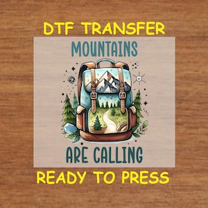 May include: A brown and blue backpack with a mountain scene inside. The text "DTG Transfer Mountains Are Calling Ready To Press" is printed on the image.