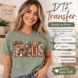 May include: A sage green t-shirt featuring the word JESUS in large, decorative letters. Each letter has a unique pattern including plaid, leopard print, and floral designs, accented with brown bows and small white daisies throughout the graphic.