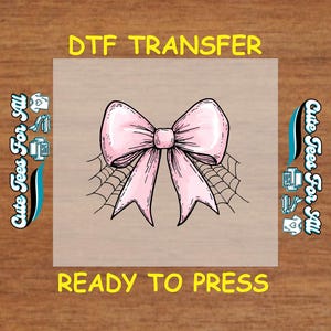 May include: A DTF transfer featuring a pink bow design with a spiderweb background. The text "DTF TRANSFER" and "READY TO PRESS" are in yellow. The words "Cute Tees For All" are on the sides.