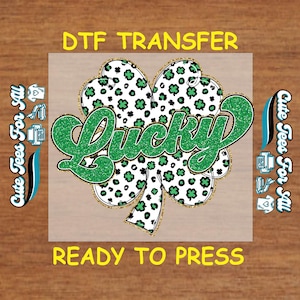 May include: A DTF transfer featuring a four-leaf clover design with a leopard print pattern in black and white. The word "Lucky" is in green glitter, and the text "Ready to Press" is at the bottom.