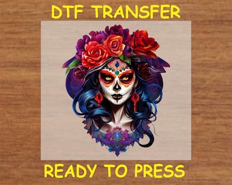 May include: A digital transfer design featuring a colorful Day of the Dead sugar skull with a floral crown. The skull has a white face with black eyes, a red nose, and a black mouth. The floral crown is made of red, orange, yellow, and purple flowers. The design is ready to be pressed onto a variety of surfaces.