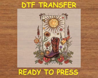 May include: A digital transfer design featuring a brown cowboy boot with a purple top, surrounded by flowers and a sun with a starburst design. The design is on a beige background and includes the text "DTF TRANSFER READY TO PRESS".