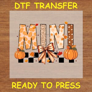 May include: A ready-to-press iron-on transfer design featuring the word "MINI" in a patchwork style with fall colors and a bow. The design includes pumpkins and leaves.