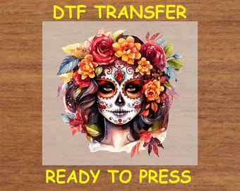 Könnte beinhalten: Ein farbenfrohes DTF-Transferdesign mit einem Zucker Schädel mit floralen Akzenten. Der Schädel hat ein weißes Gesicht mit schwarzen und roten Details, und die Blumen sind rot, gelb und orange. Das Design ist bereit, auf eine Stoffoberfläche gepresst zu werden.