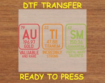 May include: A DTF transfer sheet with three colorful squares representing the elements gold, titanium, and samarium. Each square has the element's symbol, atomic number, atomic weight, and a description. The text "DTF TRANSFER" is at the top of the sheet and "READY TO PRESS" is at the bottom.