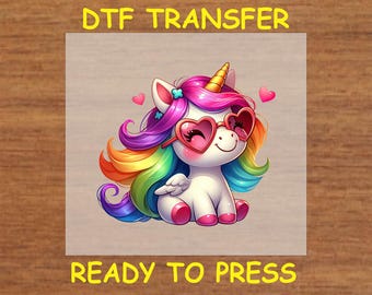 May include: A colorful rainbow unicorn with pink heart-shaped sunglasses and a pink flower in its hair. The unicorn is sitting on a white background with the text "DTF TRANSFER READY TO PRESS" at the top and bottom of the image.