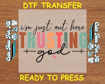 May include: A DTF transfer with the text "I'm just out here TRUSTING God" in various colors. The words "DTF TRANSFER" and "READY TO PRESS" are also present. The design includes a heart and cross symbols.