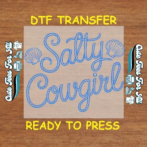 May include: A DTF transfer with the words "Salty Cowgirl" in blue rope-style lettering, accompanied by seashell illustrations. The text "DTF TRANSFER" and "READY TO PRESS" are in yellow. The phrase "Cute Tees For All" is on the sides.
