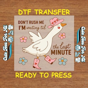 May include: A DTF transfer design featuring a cartoon goose wearing a pink cowboy hat and boots, with the text "Don't rush me, I'm waiting til the last minute." The design includes flowers and the words "Ready to press."