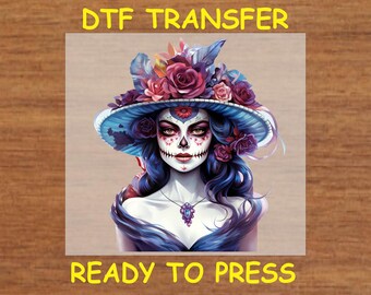 May include: A digital transfer design featuring a woman with a sugar skull makeup, wearing a blue hat with pink and purple flowers. The design is ready to press.