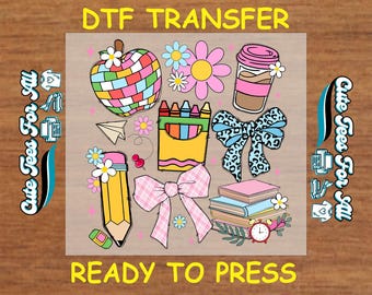 May include: DTF transfer design featuring colorful illustrations of an apple, flowers, coffee cup, bow, crayons, pencil, books, and a clock. The text "DTF TRANSFER" and "READY TO PRESS" are displayed.