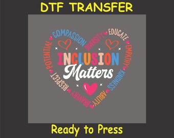 May include: A gray t-shirt with a heart-shaped design. The heart is made up of words like "compassion", "diversity", "educate", "empathy", "kindness", "ability", "bravery", "respect", and "potential". The words are in different colors and surround the words "Inclusion Matters" in the center of the heart. The words "DTF Transfer" and "Ready to Press" are also included in the image.