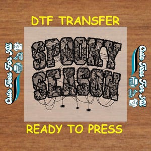 May include: A DTF transfer with the words "SPOOKY SEASON" in a black lace design. The words are connected by thin lines with small spider graphics. The text "READY TO PRESS" is below the design.