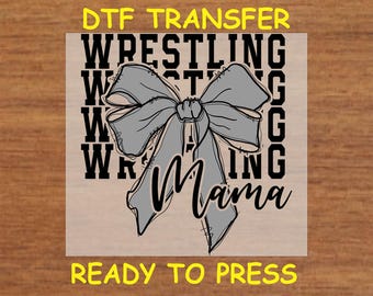 May include: A gray bow with a black outline and the text "Wrestling Mama" in black letters. The text "DTF Transfer" and "Ready to Press" are also visible in yellow letters.