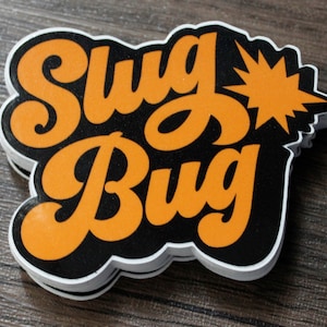 May include: A stack of black and orange stickers with the text "Slug Bug" in a retro font. The sticker has a starburst design.