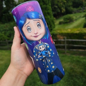 May include: A stainless steel tumbler featuring a vibrant illustration of a character with blue hair and a starry jacket. The design includes button and star motifs against a purple and blue background, creating a whimsical aesthetic.