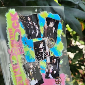 May include: A clear, rectangular sticker featuring images of a band performing. The sticker has a neon green and pink background with the words "New Kids on the Block". The images are framed in blue and black.
