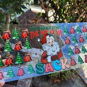 May include: A clear plastic sheet with a Christmas-themed design. It features a cartoon Santa Claus with the text "You should see the size of my sack". The design is surrounded by multiple images of Christmas trees and Santa sacks.