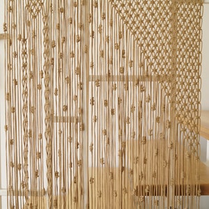 May include: A macrame wall hanging made of natural beige colored cord. The hanging features a geometric pattern with a diamond shape in the center.