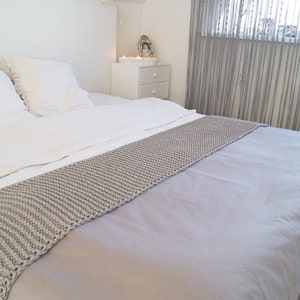 Pode incluir: Uma cama branca com almofadas brancas e uma manta de malha cinzenta.