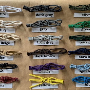 May include: A collection of 18 different colored cords tied in a knot. The cords are labeled with their color names: white, dark grey, olive, milky, grey, green, light beige, light grey, emerald, beige, dark brown, dark blue, black, purple, light blue, vinous, yellow, and blue.