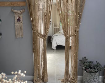 May include: A pair of beige macrame curtains with wooden beads hanging in a doorway. The curtains are made of thick rope and have a fringe at the top.
