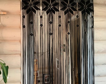 May include: Black macrame curtain with a geometric pattern. The curtain is hanging from a wooden rod.