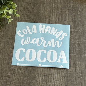 May include: White vinyl sticker on a blue background with the text "Cold Hands Warm Cocoa" and two arrows pointing in opposite directions.