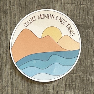 May include: A round sticker with a sunset over mountains and ocean waves. The text "Collect Moments Not Things" is written in a circle around the image.