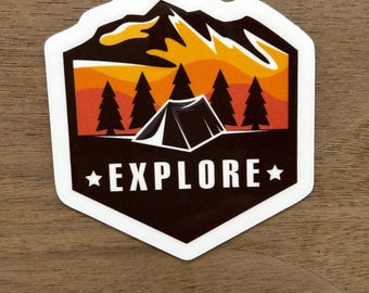 May include: A white sticker with a black mountain range silhouette, orange sunset, and five pine trees. A black tent is in the center of the trees. The text "EXPLORE" is in white with a star on either side.