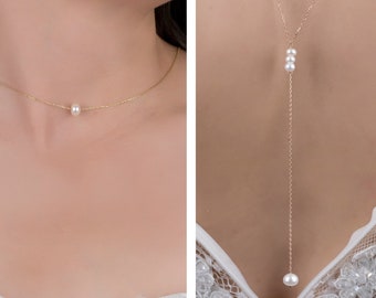 May include: Two gold necklaces with pearl accents. The first necklace is a choker with a single pearl in the center. The second necklace is a long pendant with three pearls clustered together and a single pearl at the bottom.