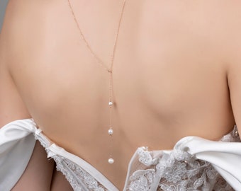May include: A delicate back necklace with a rose gold chain and three white pearls hanging from it.
