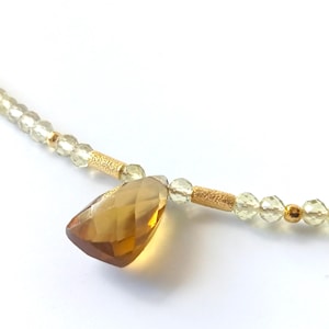May include: A gold necklace featuring a teardrop-shaped amber gemstone pendant and small, clear beads.