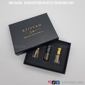 May include: A black box with the text "ATIYYAH London OPULENT OUDH FOR ALL" in gold lettering. The box is open and contains three small glass bottles with gold caps. The bottles are filled with a dark liquid.